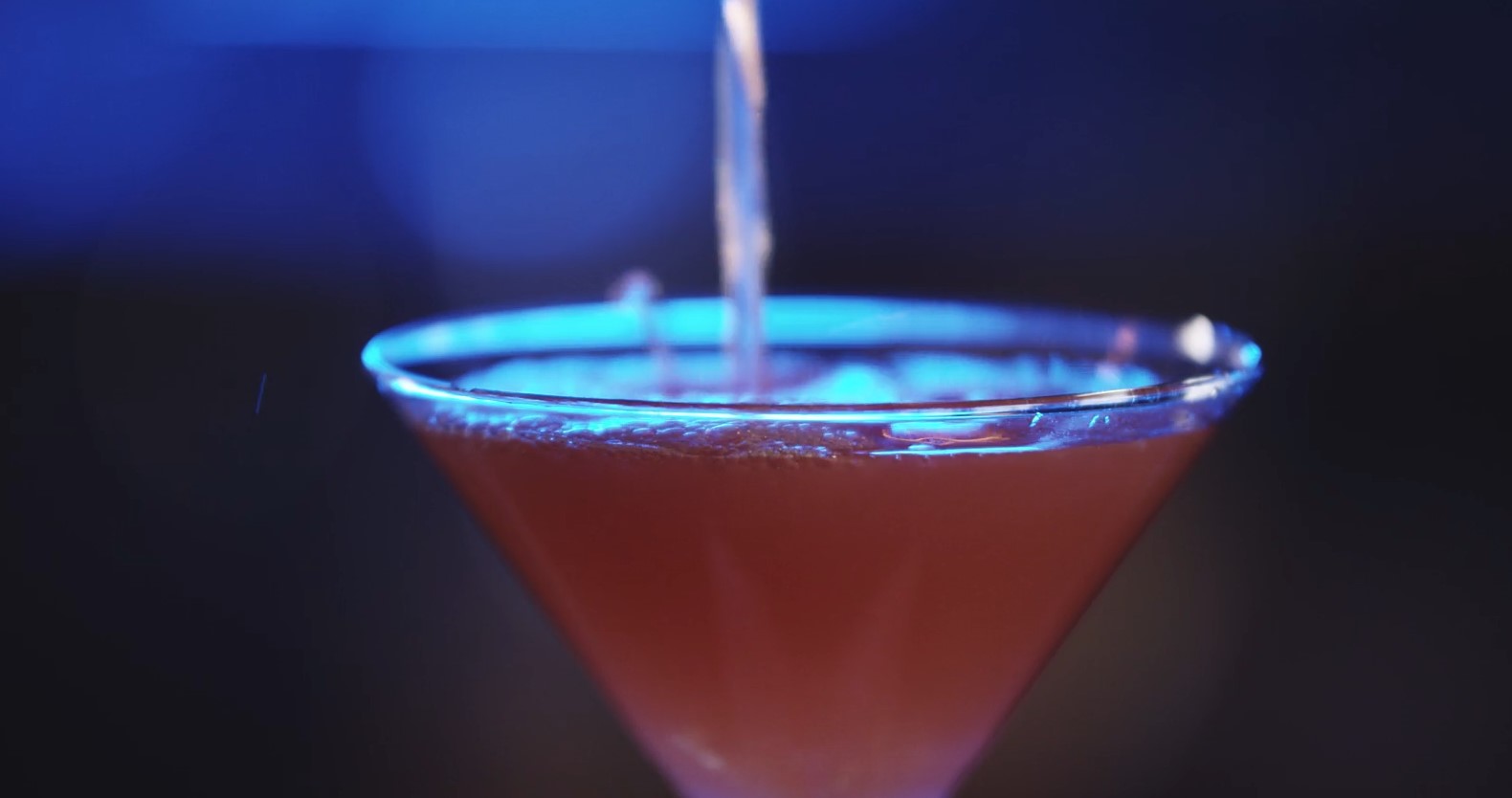 A vibrant crimson cocktail, illuminated by a cool blue light