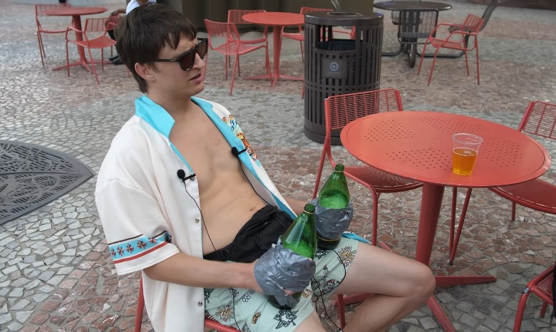 A shirtless man sitting on a chair, participating in the Edward Fortyhands drinking game with a beer in hand