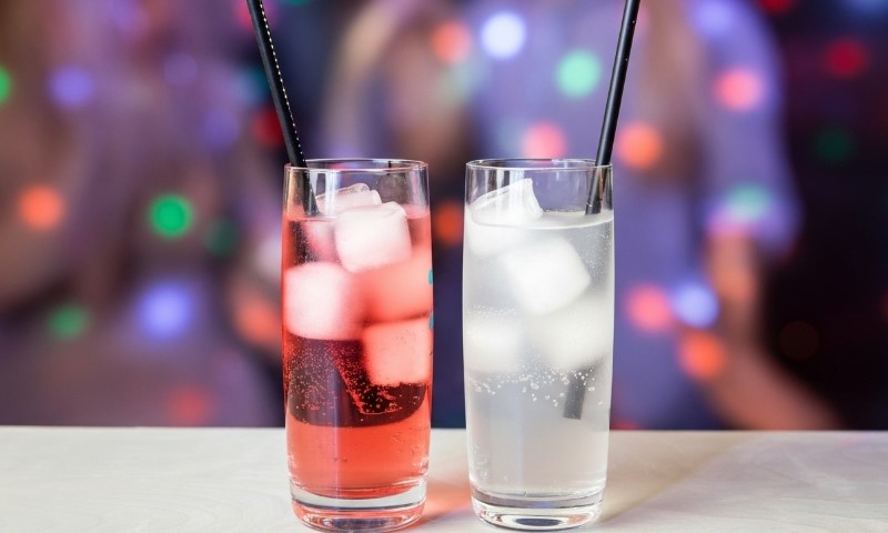 Two glasses of Chū-hai beverages filled with ice and a straw, placed on a wooden table