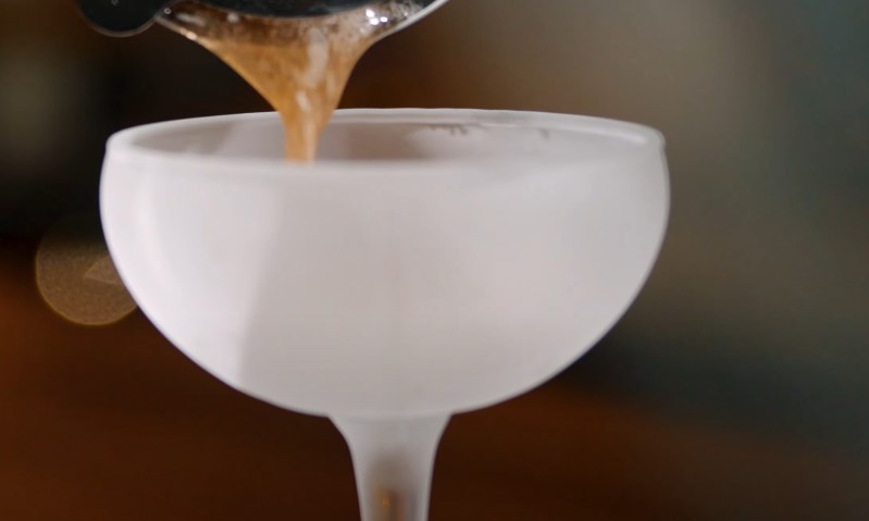 A person pouring a clear liquid from a bottle into a glass on a table