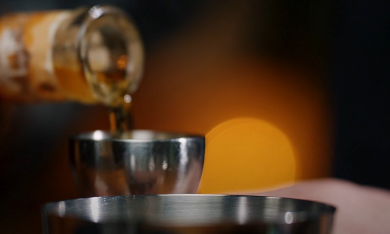 A person pouring a beverage from a bottle into a clear glass on a table