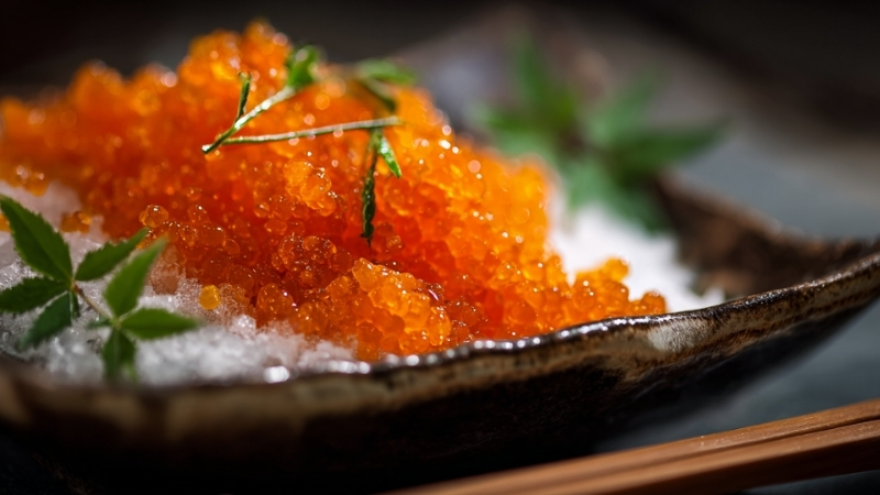 Bright orange masago roe served on ice with green garnish in a ceramic dish