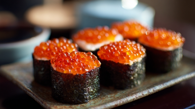 Gunkan-style sushi topped with bright orange masago roe on a ceramic plate